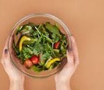 Healthy fresh salad bowl with cherry tomatoes and greens held by hands on a brown surface.