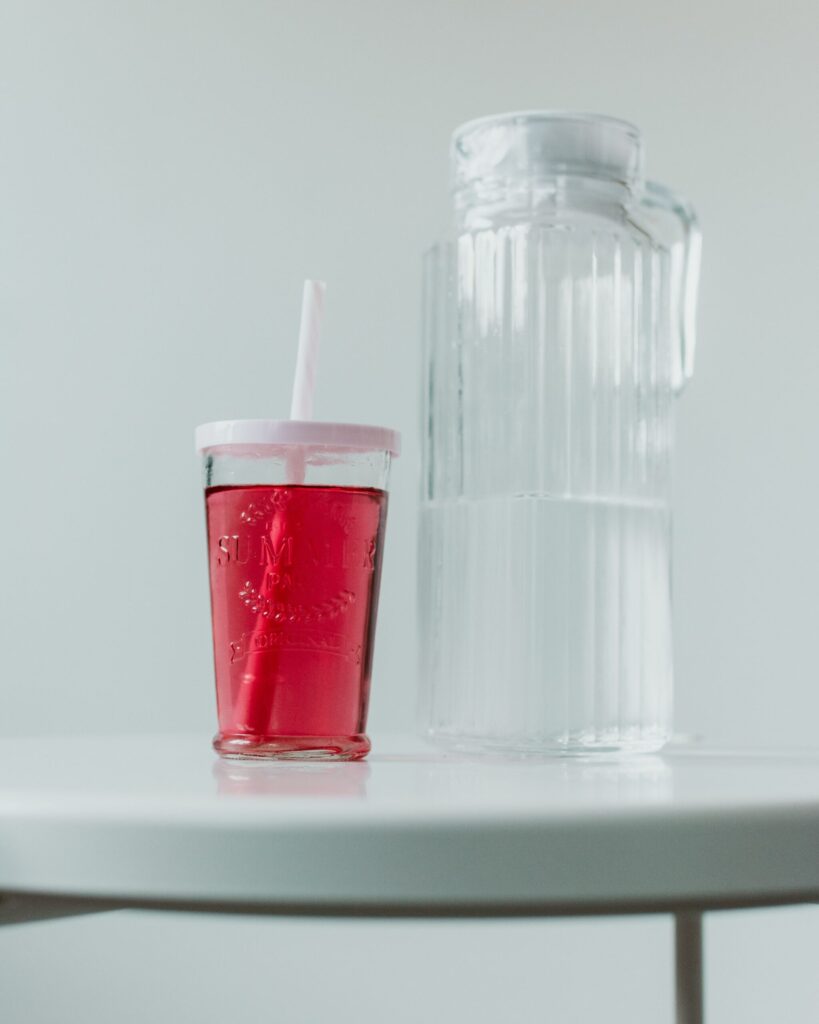 Minimalist image of a red drink in a glass cup with a clear water pitcher.