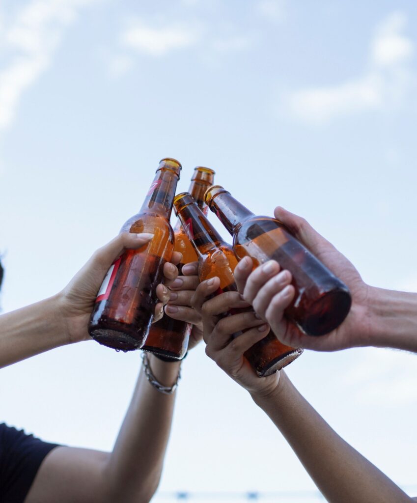 Hands raising beer bottles in a celebratory toast underneath a clear sky.
