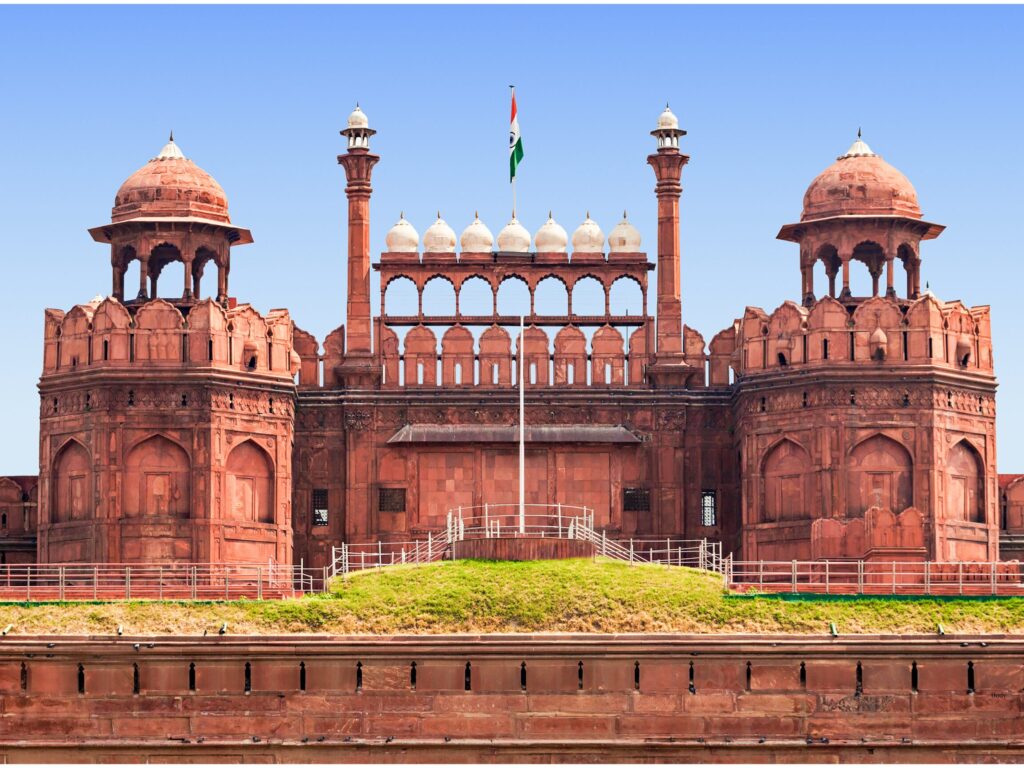 Red Fort in Delhi with red sandstone walls, open grounds, patchy grass, and visible signs of wear.
